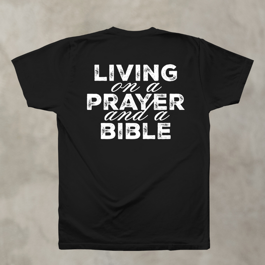 Black t-shirt with white text 'Living on a Prayer and a Bible' on a beige background